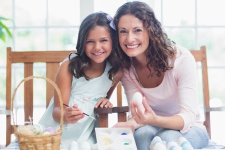 Happy mother and daughter painting easter eggs in the living room